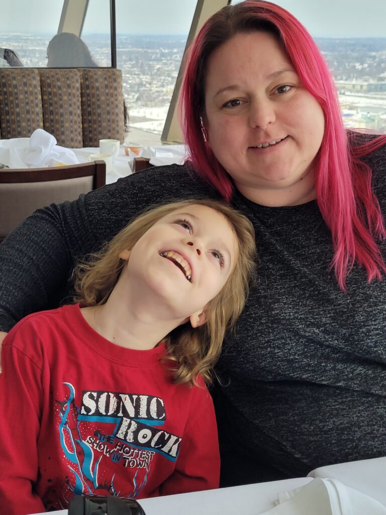 Alden (left) - a young boy with blonde hair sits beside his mom, Natasha (right).