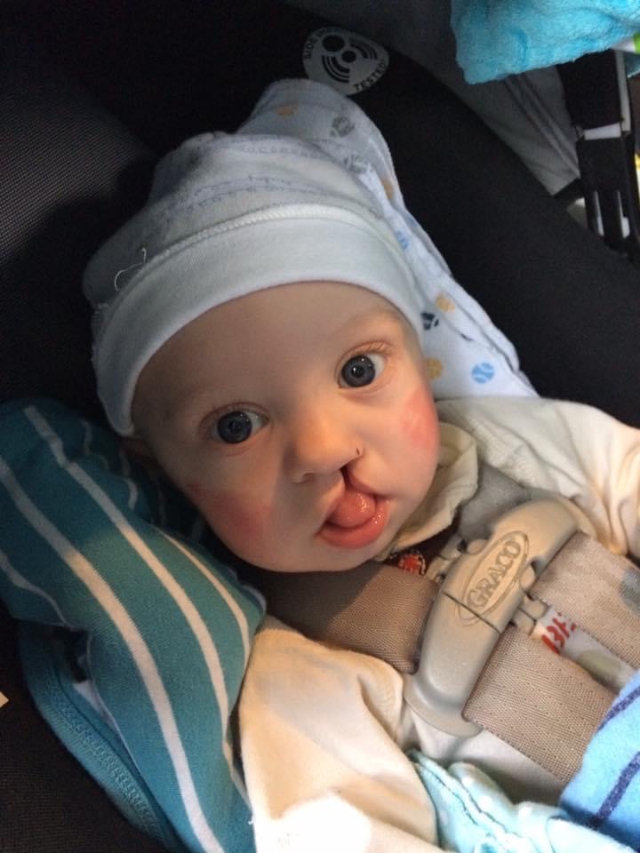A baby Charlie in a car seat wearing a white hat. 