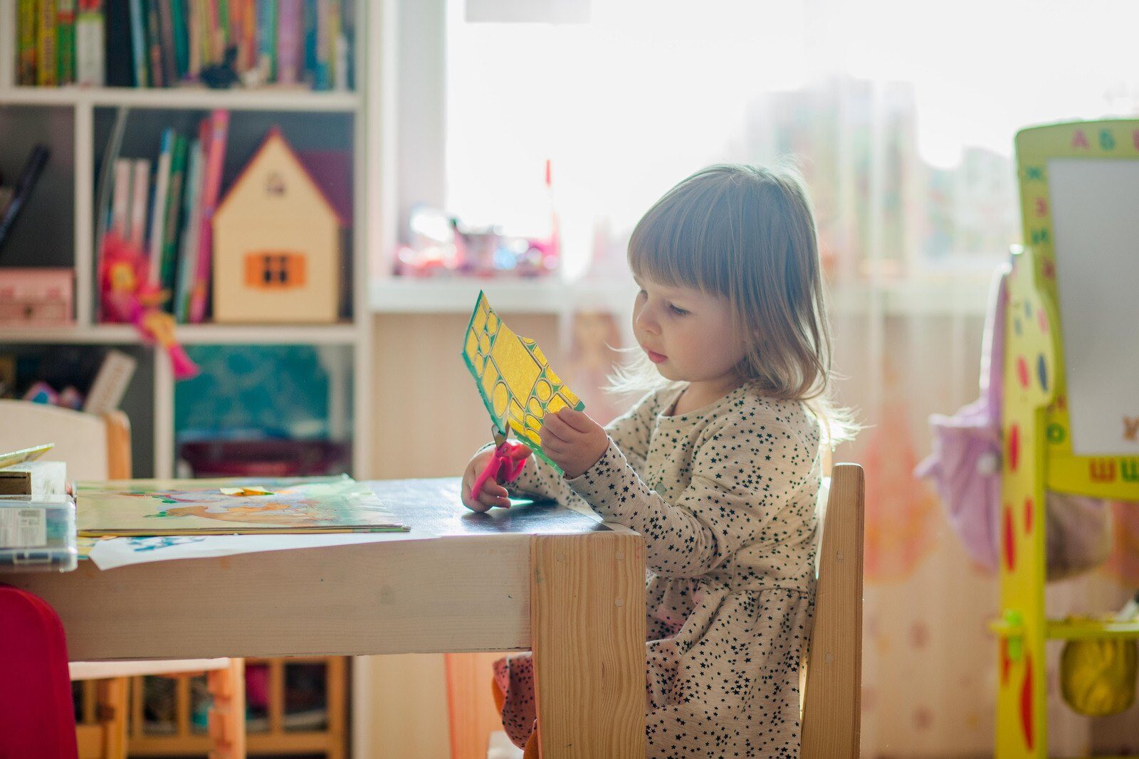 Toddler girl cutting paper with small pink scissors.