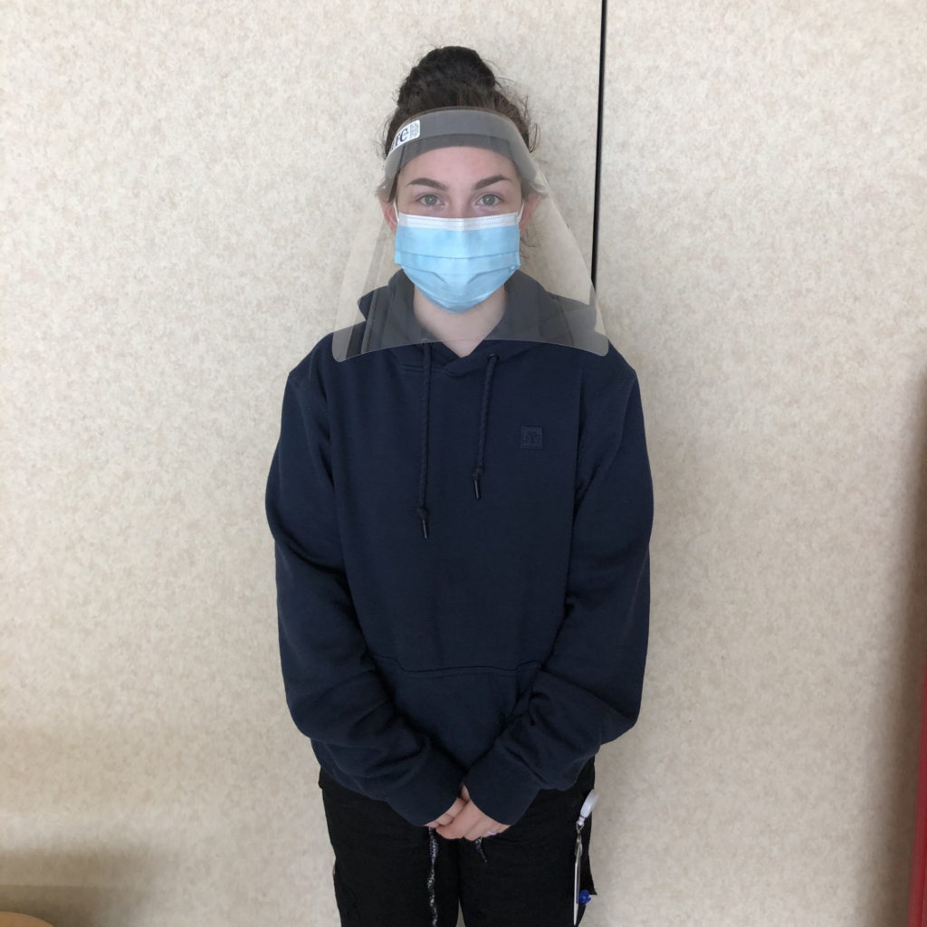 Photo of placement student, Aurora, donned in Personal Protective Equipment, which includes a blue dispoable face mask and a face shield.