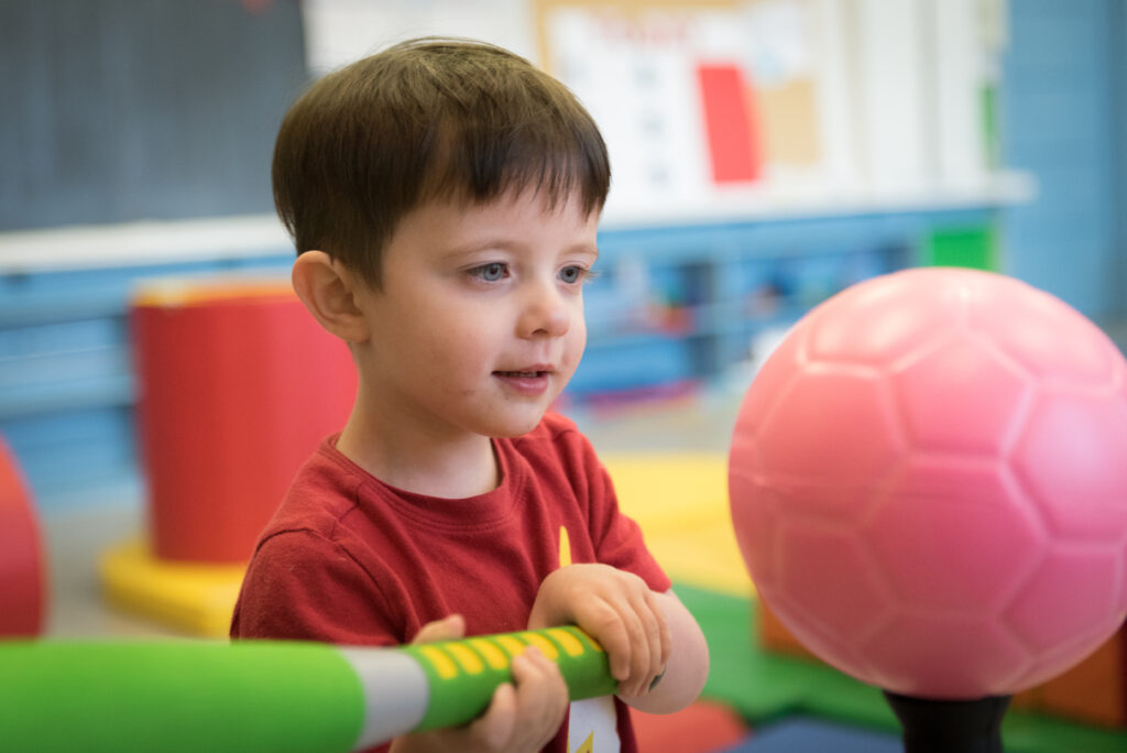 Little boy holding a toy bat up to a softball in Dr. Meghann Lloyd's lab.