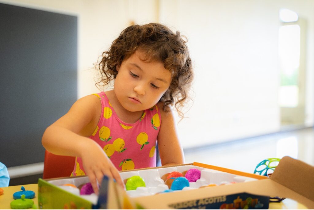 Little girl playing with curly brown hair playing with colourful toys on a table.