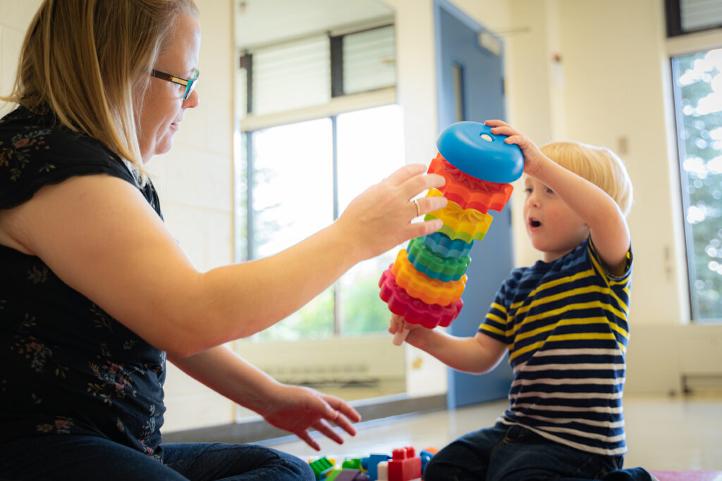 Little boy and his mom in a Grandview Kids Therapy Room playing with a rainbow-coloured toy.