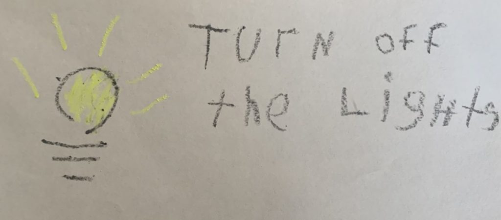 A child's drawing of a light blub with "Turn off the lights" written in black crayon.