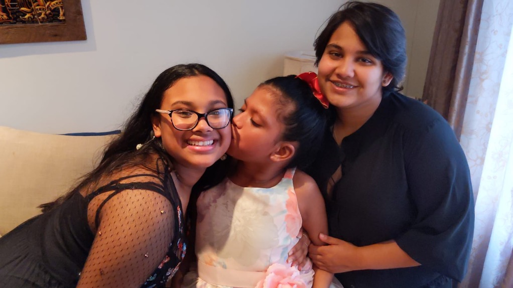 Kayden sitting in-between her two siblings while kissing her sister to the right of her on the cheeck.