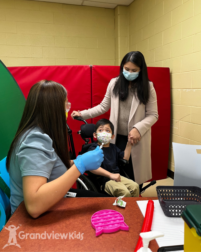 A little boy holding his mother's hand while waiting to be vaccinated by a nurse at the Grandview Kids vaccine clinic.