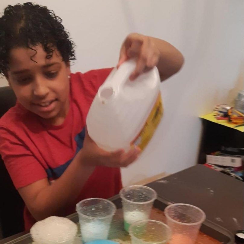 Child pouring vinegar into colourful baking soda volcanoes in plastic cups.