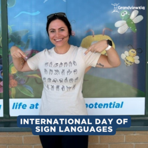A female with dark hair, pointing to her white t-shirt which has sign language gestures.