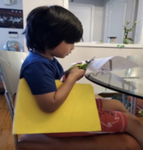 Boy cutting paper with green scissors.