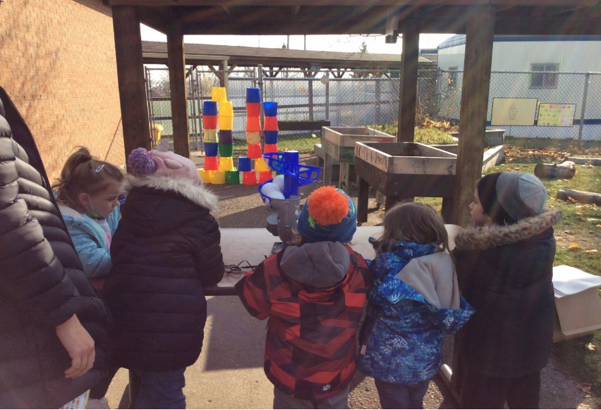 Students using a switch-adapted pitching machine to knock down a tower with a ball without having to physically throw the ball.