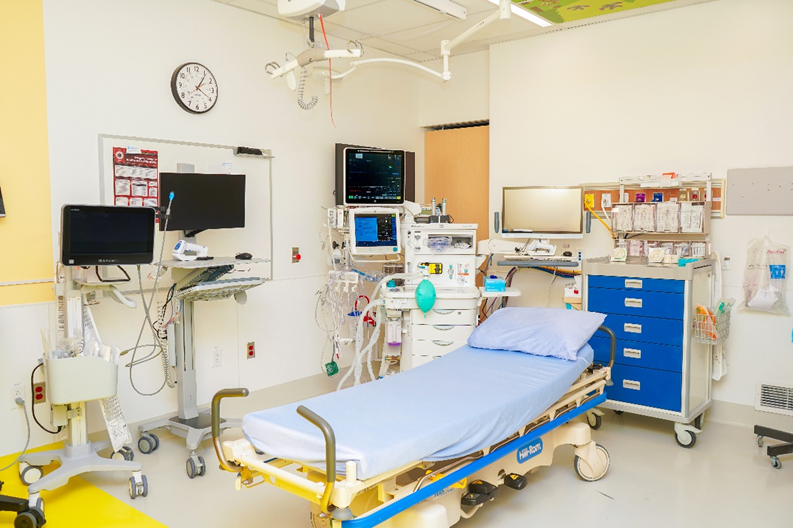 The GAP Clinic’s procedure room, showcasing its equipment, including a bed, anesthesia gas machine, rolling carts and other technological equipment, like computers on rolling stands.