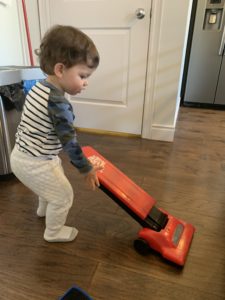 A young child playing with an orange toy vacuum clearner.