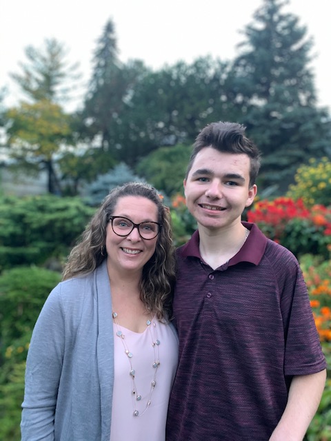 Portrait photograph of Owen DiManno posing beside his mother, Rebecca, in front of a lush garden.