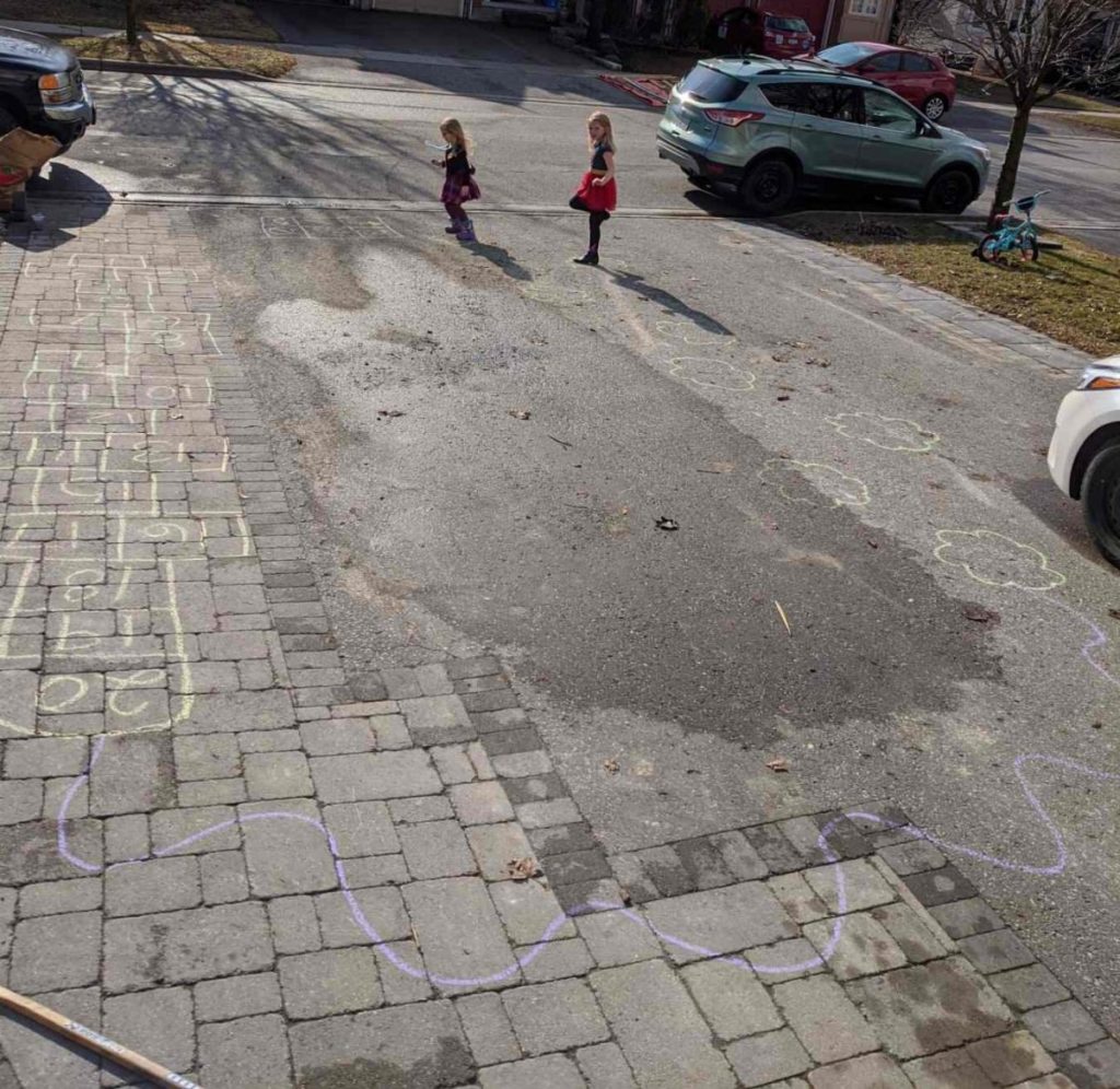 A picture of two children doing a sidewalk chalk obstacle course.