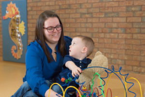 Mother holding her son while he plays with various toys.