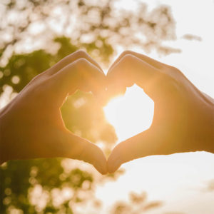 Person making a heart with their hands over the sun